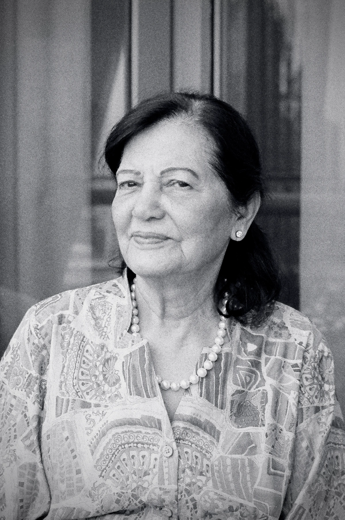 2/2: A black and white portrait of my grandmother, smiling gently while wearing a patterned blouse and a pearl necklace, with a calm and content expression.