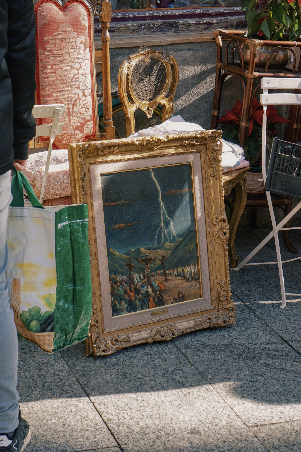 An ornate framed painting depicting a biblical scene with a thunderstorm, displayed among vintage furniture at an outdoor market.