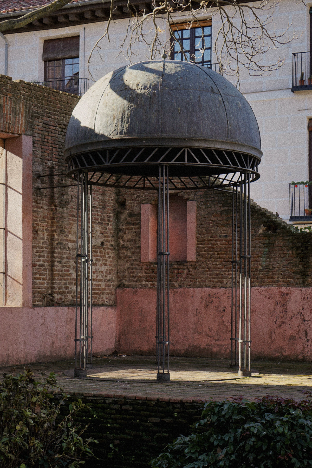 A small domed pavilion supported by slender iron columns, set in a courtyard with brick and plaster walls.
