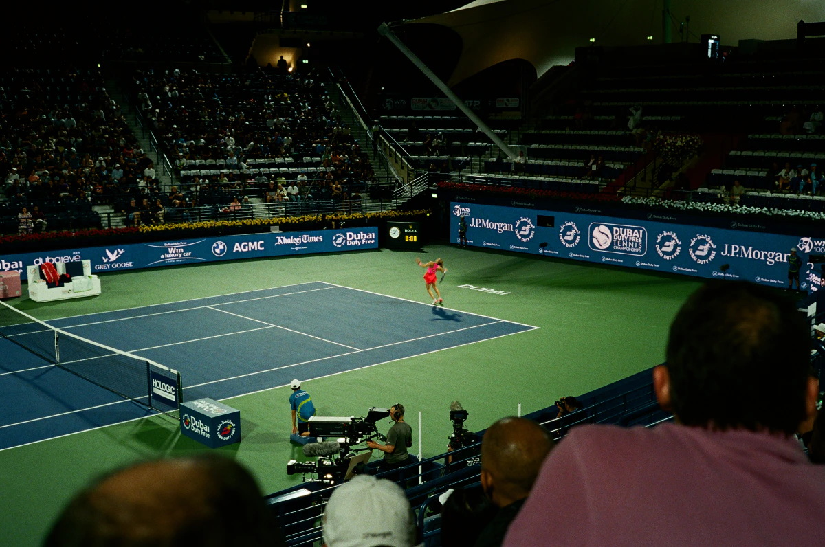 Maria Sakkari, in a bright red outfit, serves during a match at the 2025 Dubai Tennis Open. The crowd watches from the stands as the player moves with precision under the stadium lights.